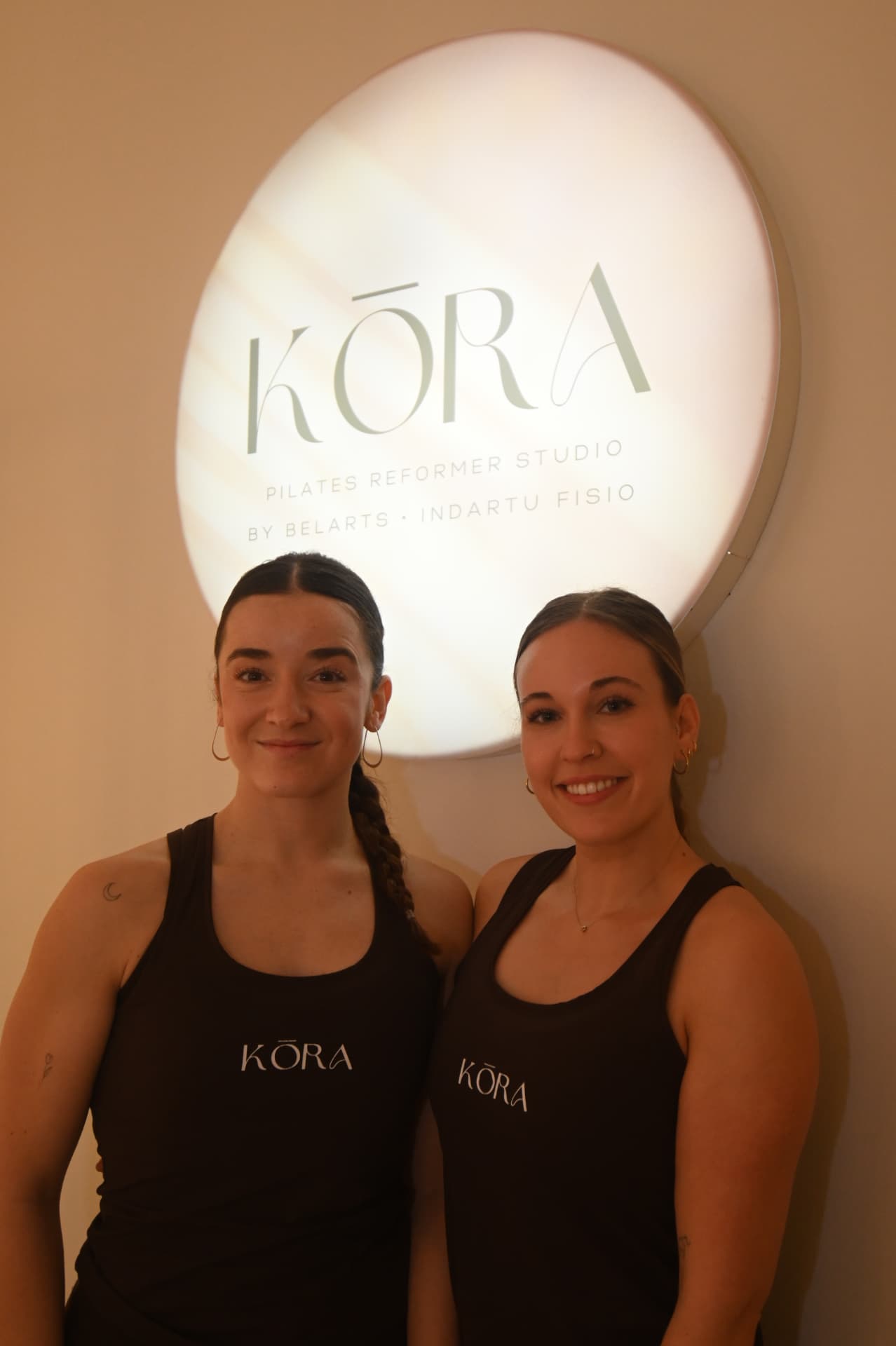 Sayoa Belarra y Lore Bergara con camiseta de KŌRA delante del rótulo iluminado del estudio