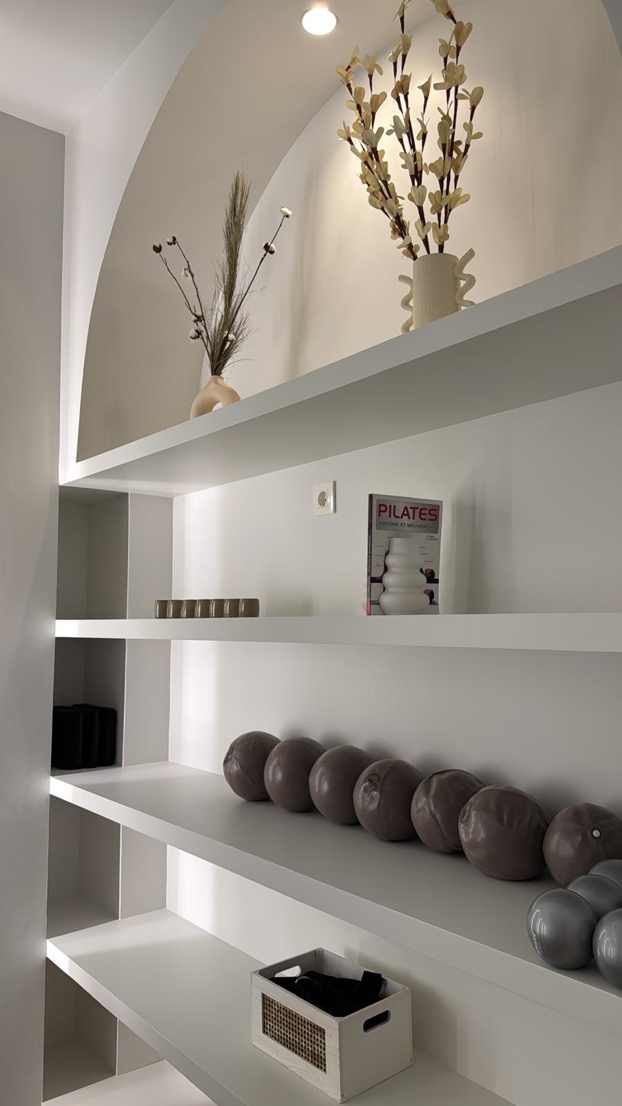 Estanterías blancas del estudio con pelotas de Pilates, aros y plantas secas