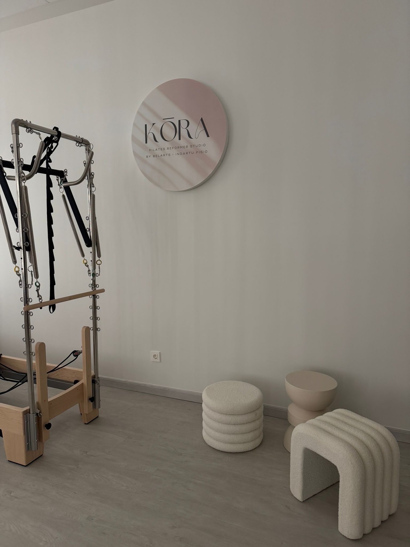 Rincón de espera con banquetas de bouclé bajo el rótulo circular de KŌRA