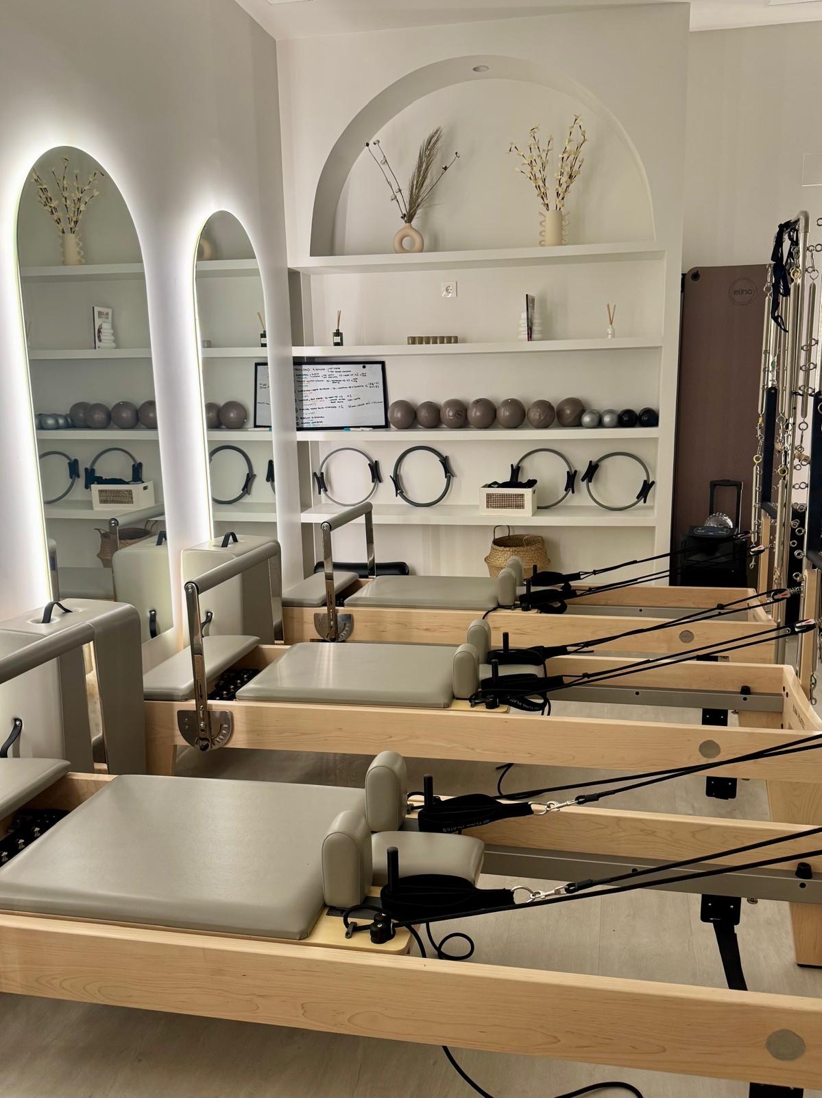 Sala del estudio con reformers alineados, espejos con arcos y estanterías con material de Pilates